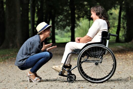 Woman in wheel chair and man crouched in front of her in park