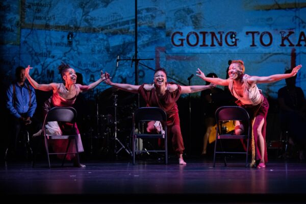 Three women dance in front of musicians