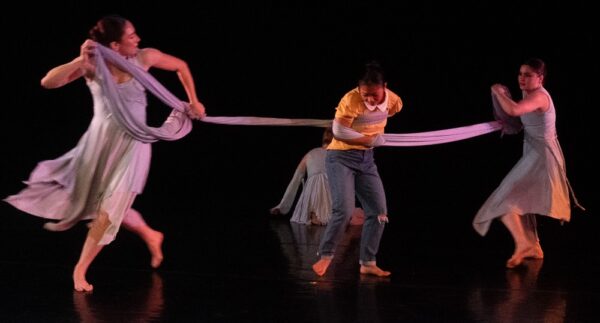 Dancers hold scarf around another dancer