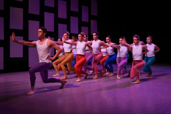 A group of dancers in white shirts lunge