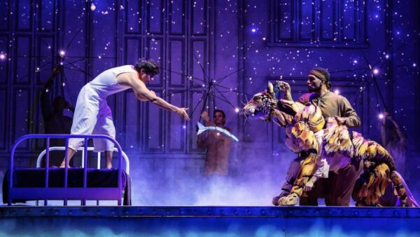 A dancer in white leans toward tiger pupper