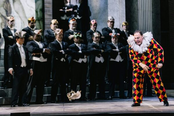 A clown in front of a line of men with masks in Rigoletto