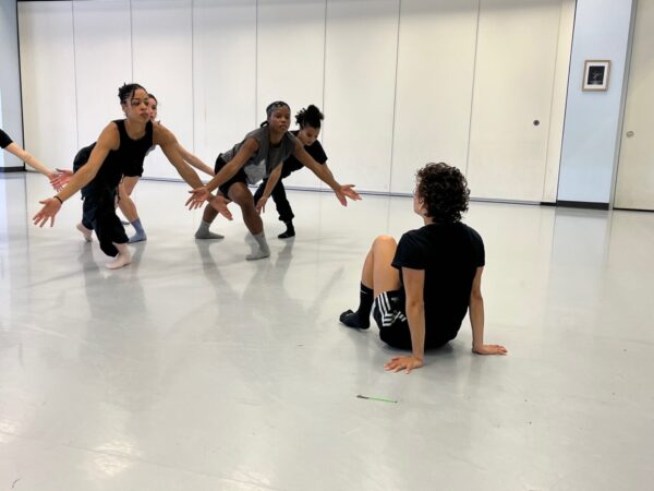 A dancer sits on floor facing a group