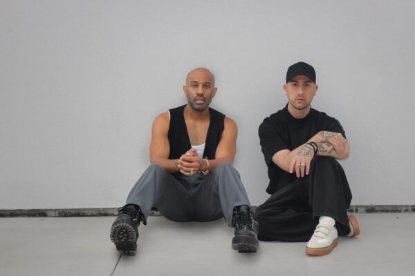 Two men sit with backs to wall