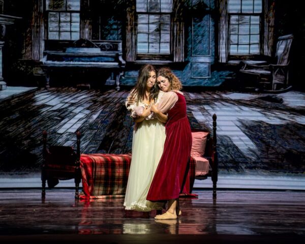 A woman in white is hugged by a woman in red