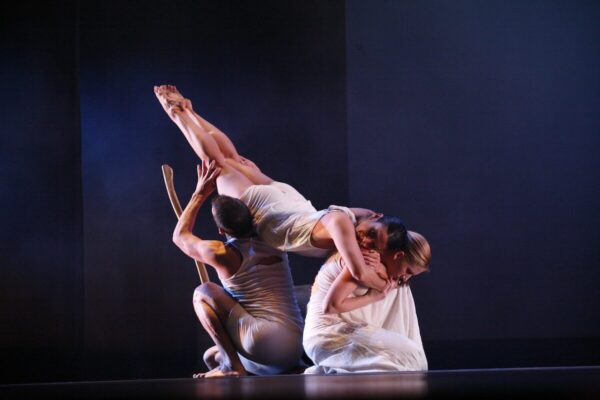 A dancer in white held at angle by other dancers