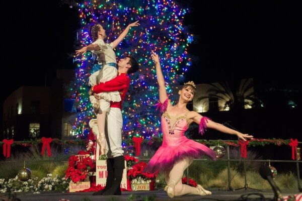 A dancer kneels while another lifts a girl in white