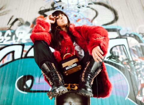 A woman in a red fur coat sitting on a skateboard