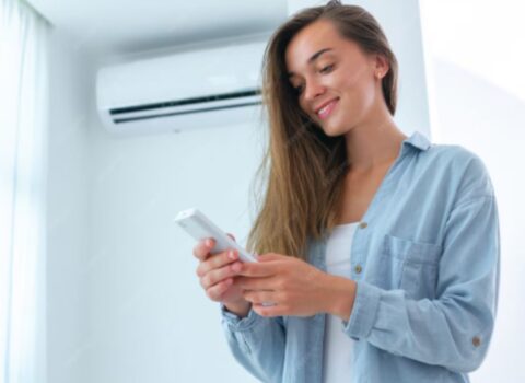 Young attractive woman control air conditioner temperature using remote controller in room at home.
