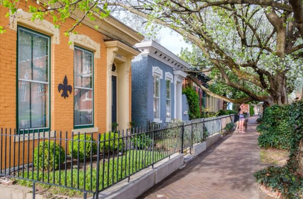Shotgun homes in Butchertown - one is orange, the other light blue. There are small bushy gardens in front of the homes linked with a black metal fence. 