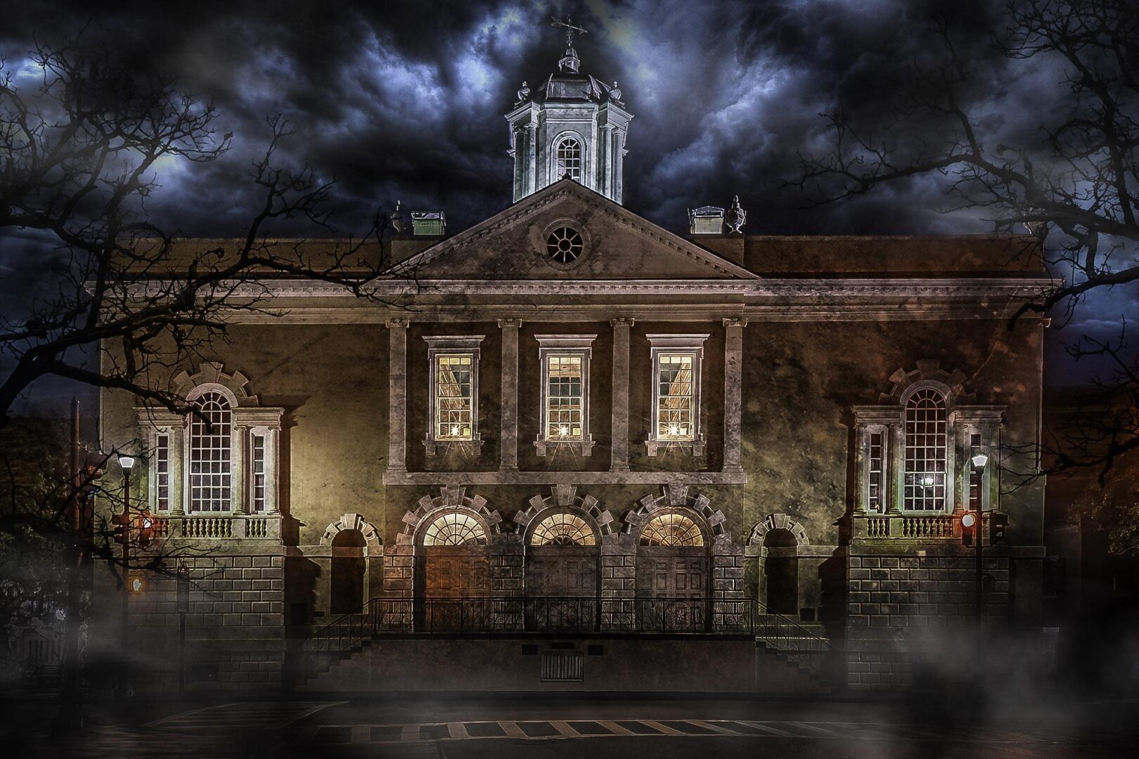 Illuminated colonial brick building with cupola and arched windows under stormy night sky