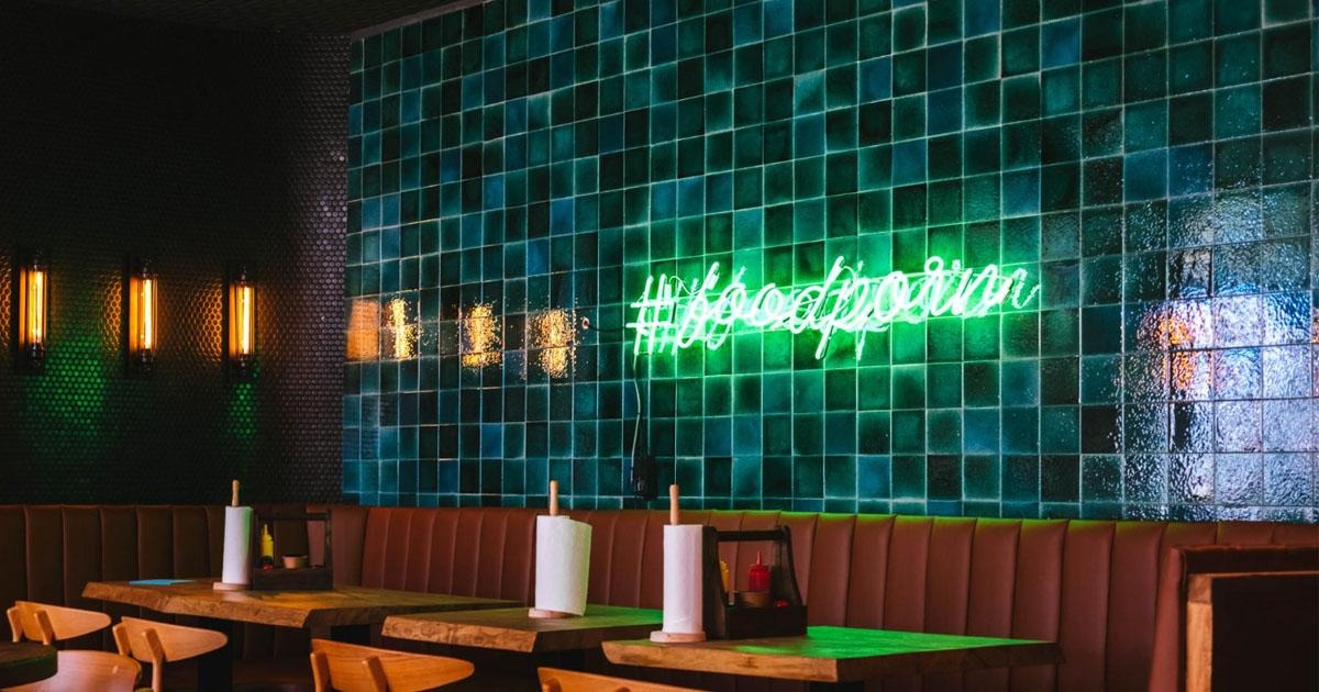Green tiled restaurant wall with a glowing hashtag foodporn sign above empty booths