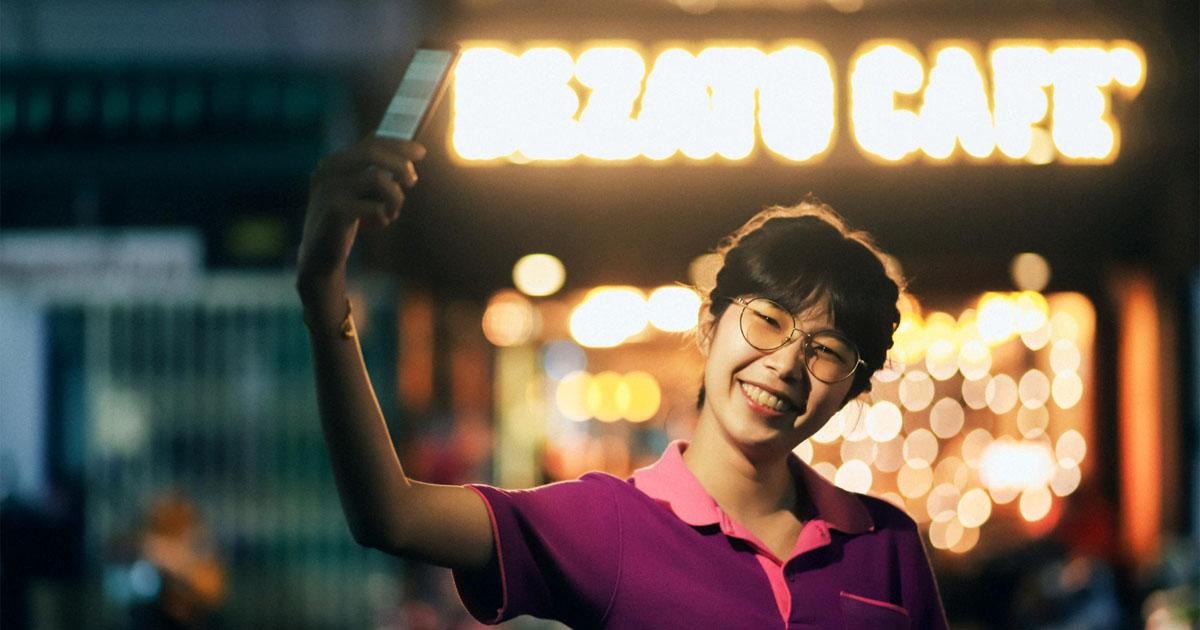 Smiling young woman taking a selfie outside a glowing cafe sign at night