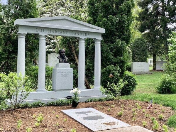 Col Sanders burial memorial at Cave Hill Cemetery showing four columns topped by a triangular top. The grave is before the structure. 