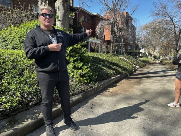 Author David Dominé gives walking tours of Old Louisville. he stands on a sidewalk before Victorian homes, pointing out one of them. 