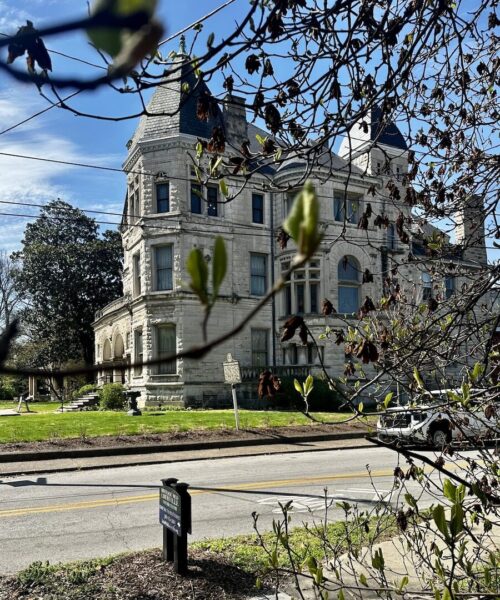 A stone Victorian home - The Conrad-Caldwell House designed by Clarke & Loomis architects. It is very large, built of a white stone with peaked roofs on the corners. 