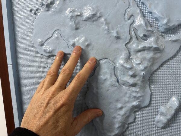 Fingers touching a tactile map of Africa that's a grey color