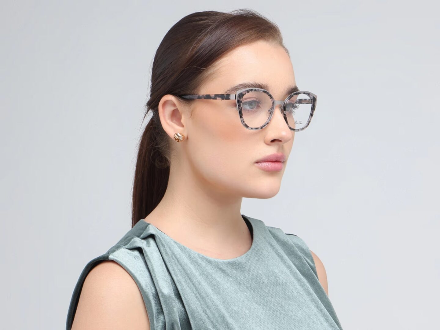 Woman with brown hair wearing wide angular tortoise-shell patterned frames and a sage green sleeveless top