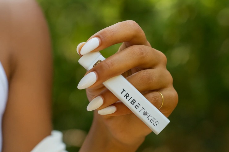 Close-up of a hand with long white nails holding a small white branded pen device outdoors
