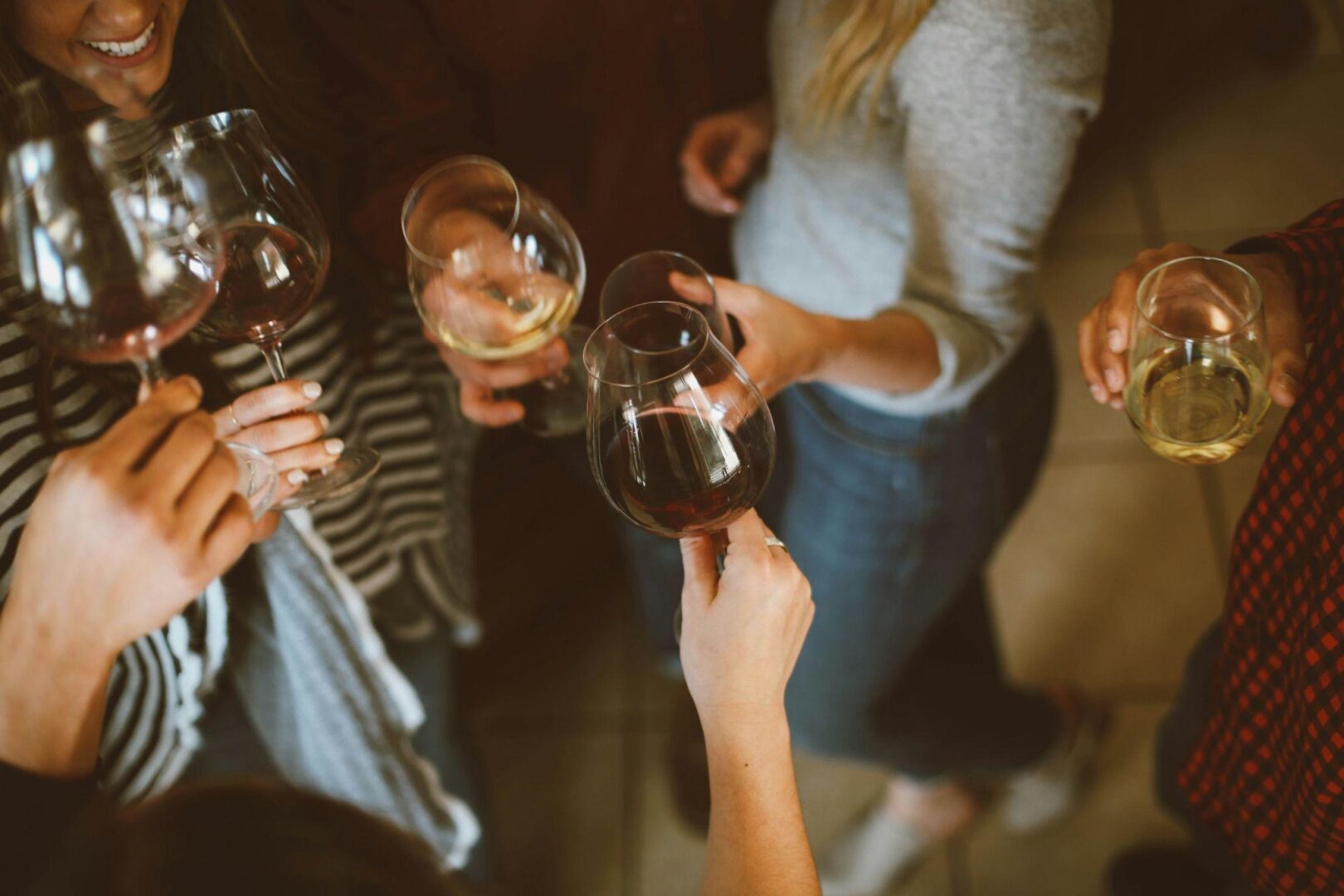 Several people holding wine glasses with red and white wine, clinking them together indoors