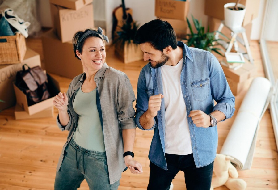CD-Insert1 A smiling woman and man dancing on a wood floor surrounded by labeled cardboard moving boxes