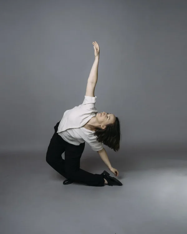 A dancer in a white shirt lifts her arm