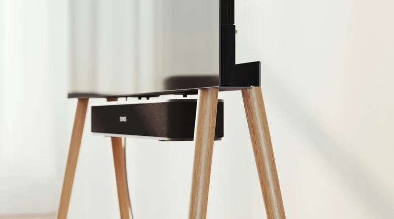 A flat screen display mounted on a wooden easel-style stand with light wood legs against a white wall