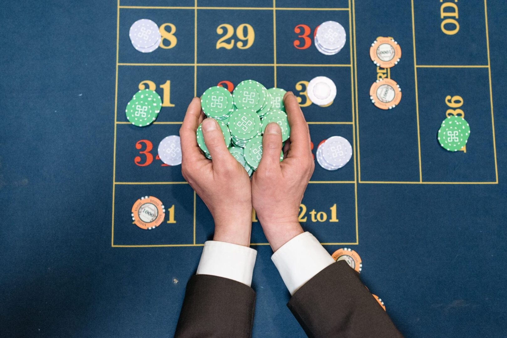 CD-Insert1 Overhead view of hands in a suit gathering green poker chips on a blue roulette table