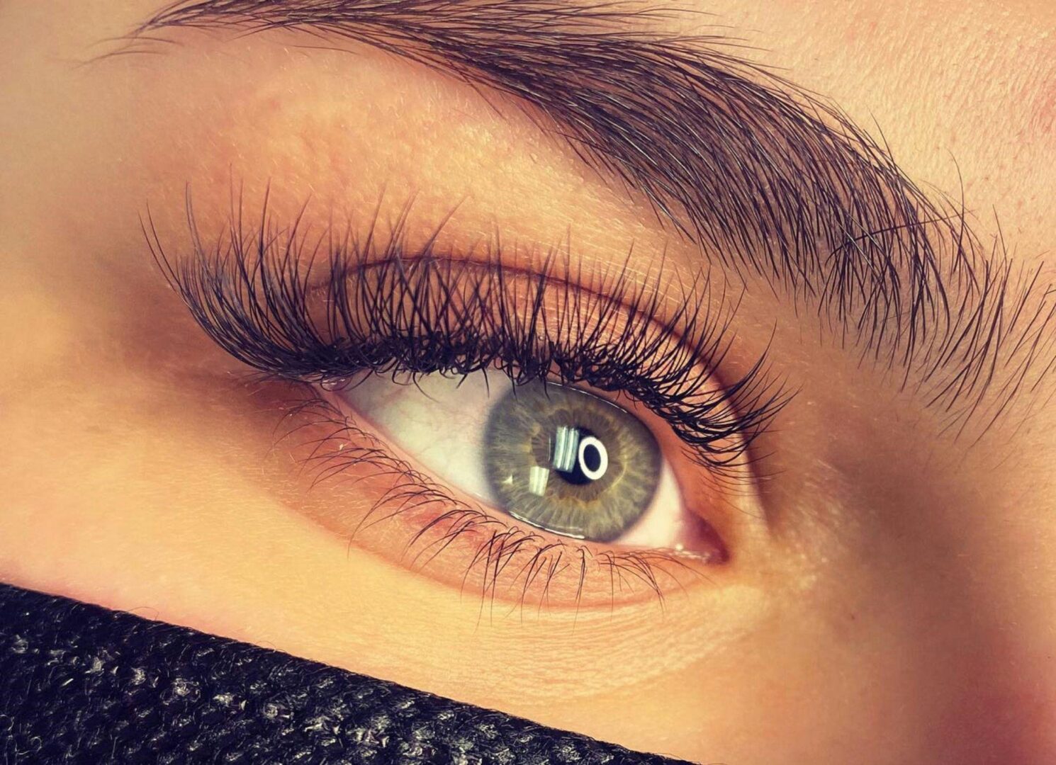 CD-Insert1 Close-up of a green-gray eye with long dark lashes and a groomed brown eyebrow