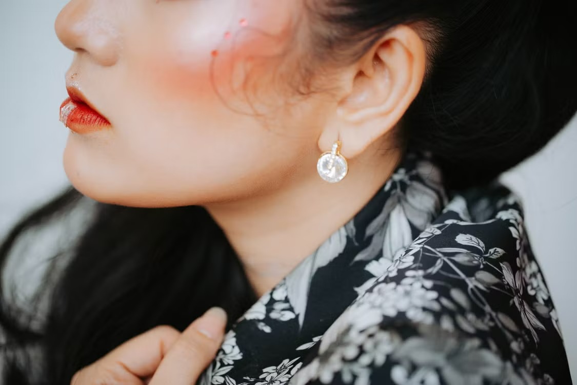 CD-Insert1 Close-up of a woman wearing a round crystal drop earring, red lipstick, and a dark floral top