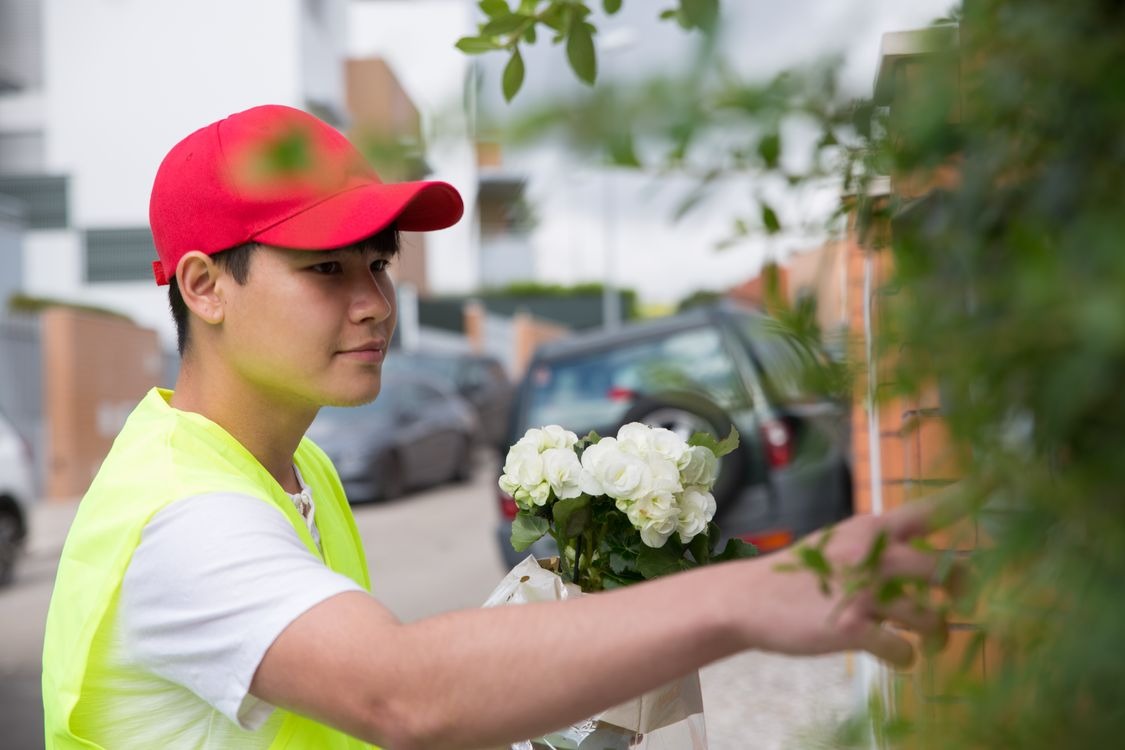 Young man in red cap and yellow vest holding white roses near a gate outdoors