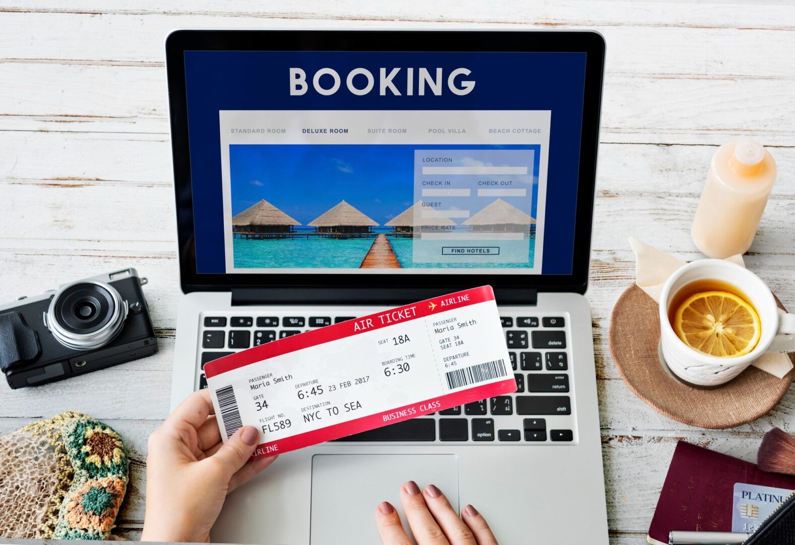 CD-Insert2 Hand holding a red airline ticket over a laptop showing a hotel booking website with a camera and tea cup nearby