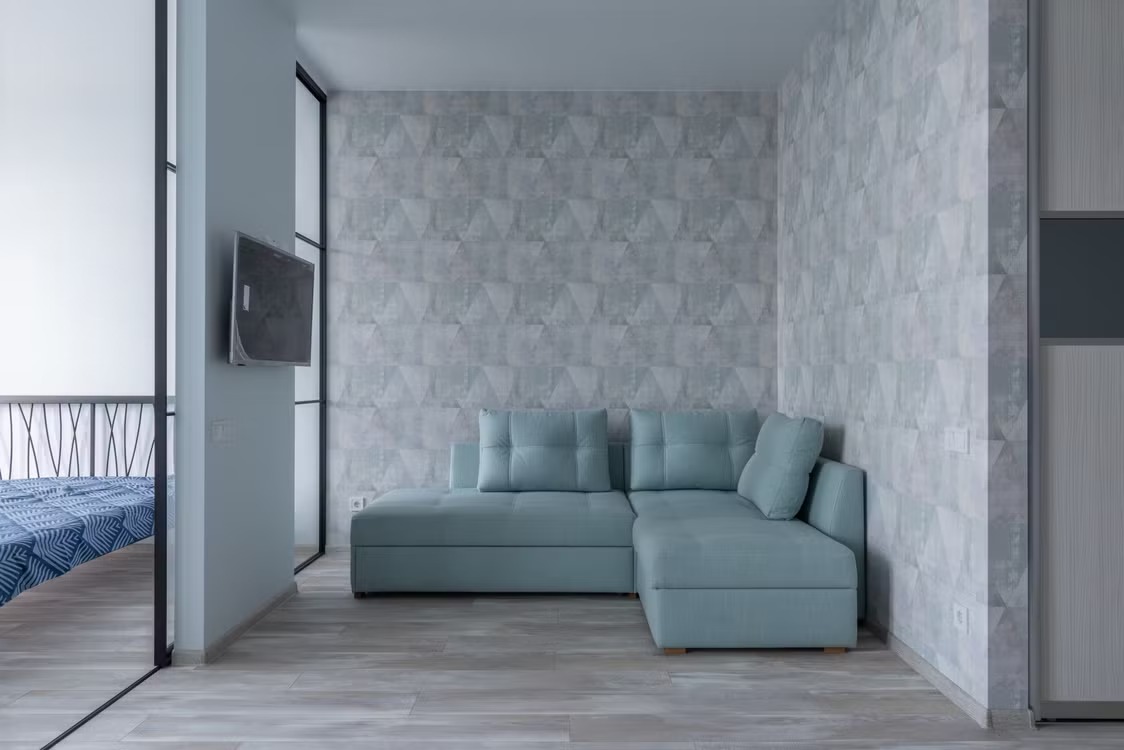 CD-Insert1 Light blue L-shaped corner sofa against geometric gray wallpaper in a modern room with tiled floor