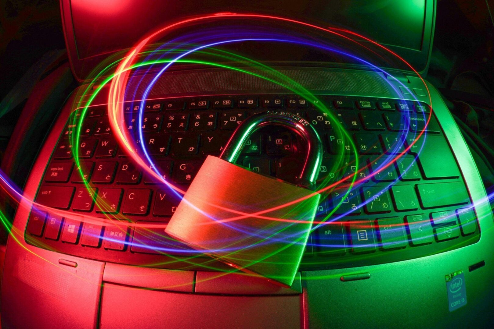 CD-Insert1 A padlock sitting on a laptop keyboard with colorful light trails swirling around it in red green and blue