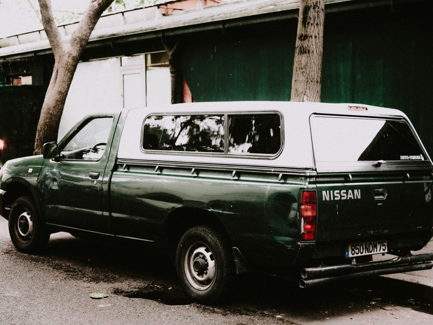 CD-Insert2 Green pickup truck with a white canopy shell parked on a city street