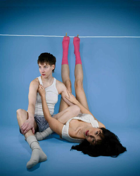 One dancer sits on floor, second dancer lifts legs