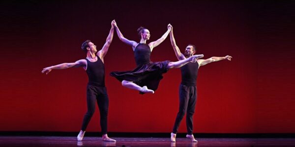 A female dancer is lifted by two male dancers