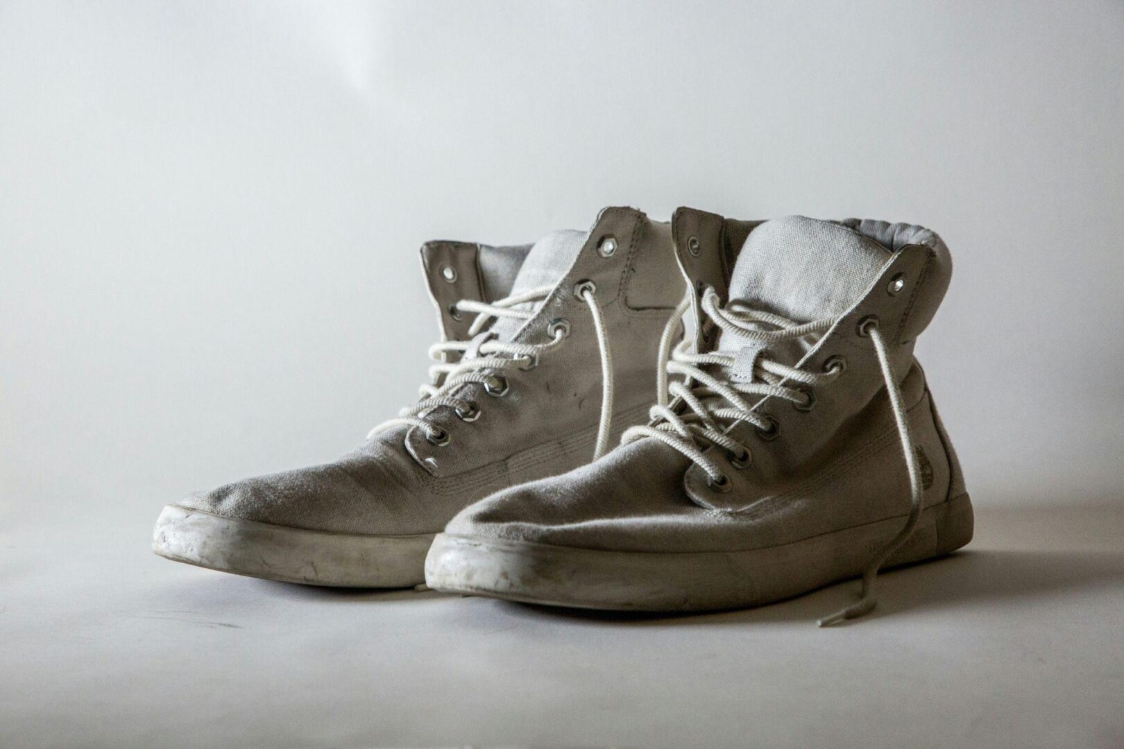 CD-shoe-wardrobe-refresh-Insert1 A pair of worn, dirty white high-top canvas sneakers with white laces on a light gray surface