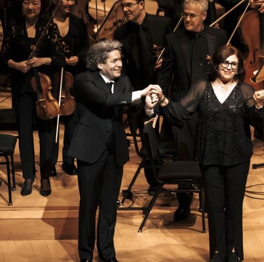 A man holds a woman's hand in front of an orchestra
