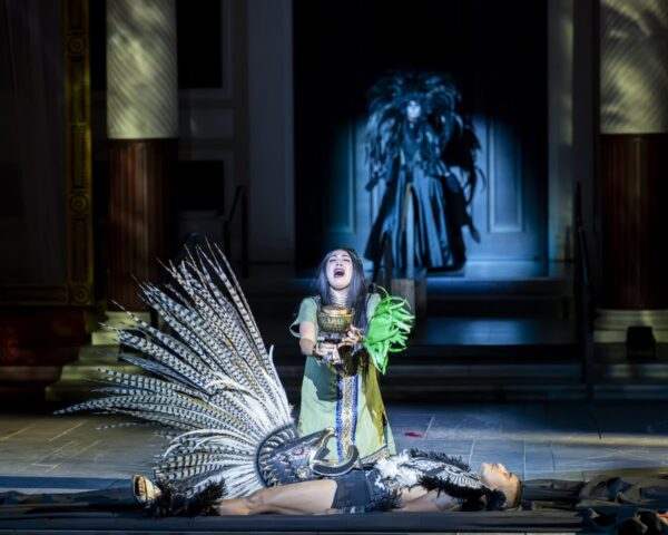 A woman kneels before a figure with feather