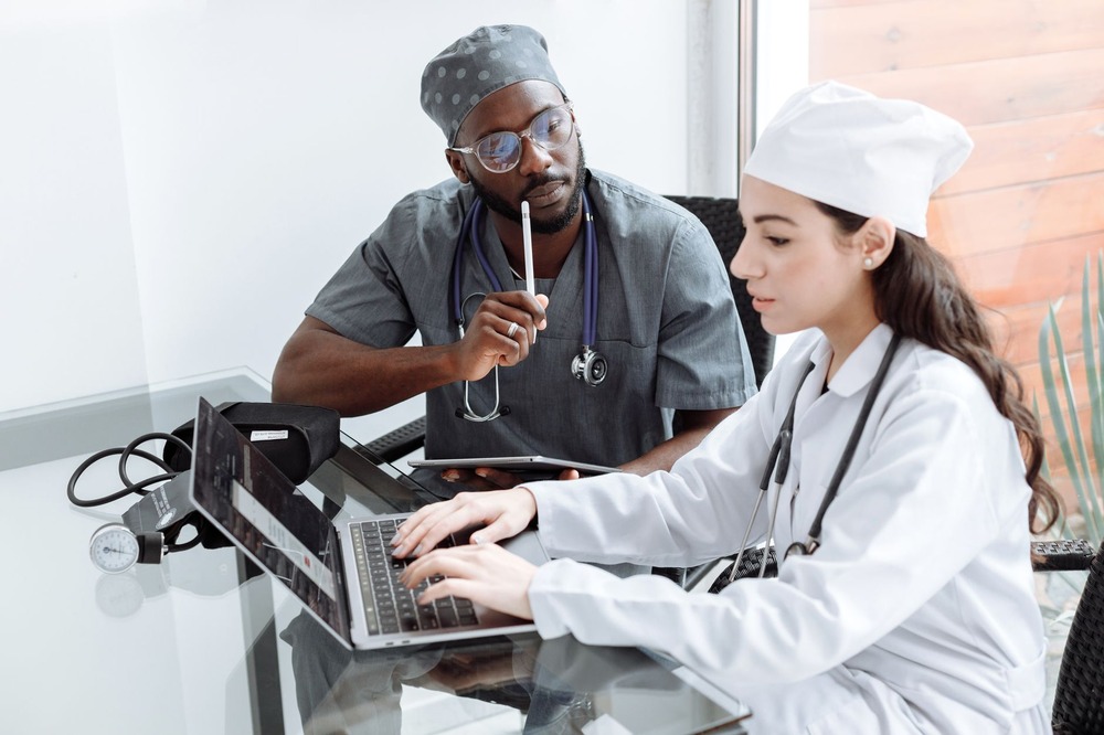 CD-healthcare-virtual-assistant-Insert4 Two medical professionals in scrubs discussing work on a laptop