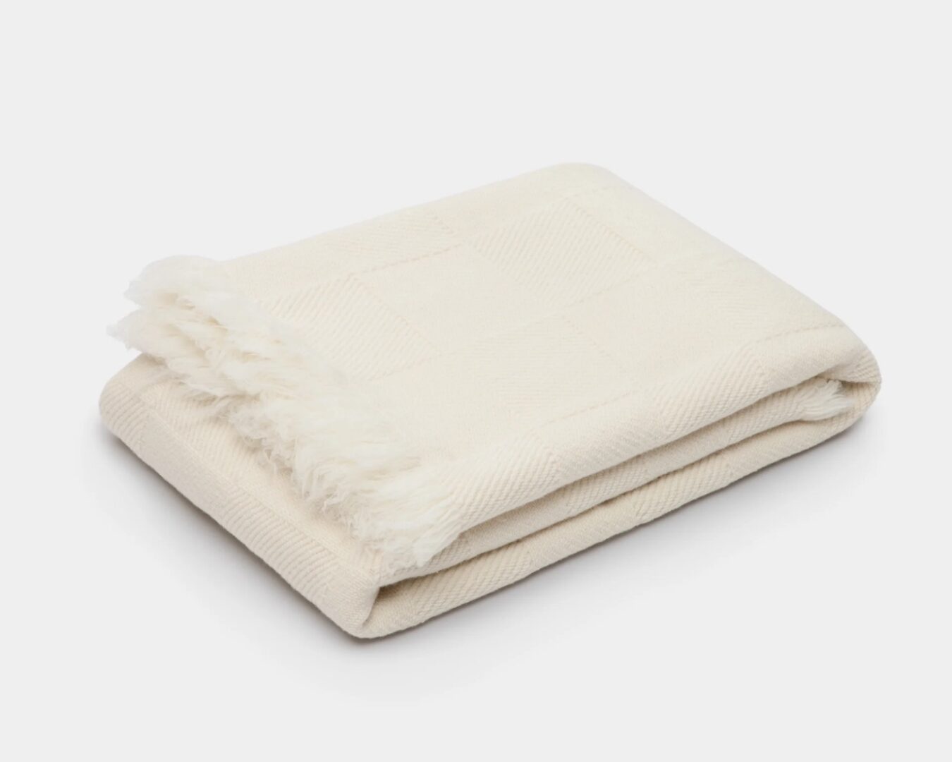 CD-Insert1 Folded cream woven throw with fringe edges on a white background