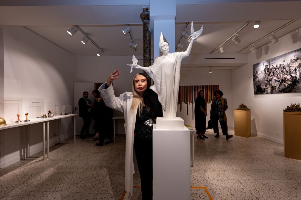 CD-Insert1 Woman in a long white coat standing beside a white statue of a woman holding two doves