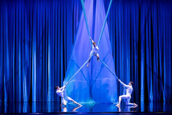 Two acrobats hold a third with poles