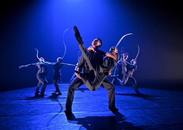 A dancer holds another who extends leg
